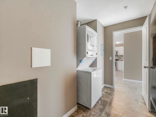 Dedicated laundry area featuring a stacked washer and dryer, tile flooring, and neutral wall tones - 322 1520 Hammond Gate Nw, Edmonton, AB - Indoor Photo Showing Laundry Room