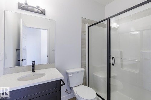 Bathroom featuring a dark vanity with a light countertop, a rectangular mirror, and a walk-in shower with a black-framed glass enclosure - 6275 180 Avenue Nw, Edmonton, AB - Indoor Photo Showing Bathroom