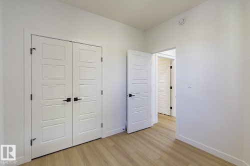 Room featuring wood-finish flooring, crisp white walls, and contemporary paneled doors with matte black hardware - 6275 180 Avenue Nw, Edmonton, AB - Indoor Photo Showing Other Room