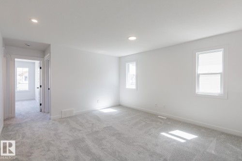 Spacious room featuring light gray patterned carpeting, recessed ceiling lighting, two windows with white trim, and white painted walls - 6275 180 Avenue Nw, Edmonton, AB - Indoor Photo Showing Other Room