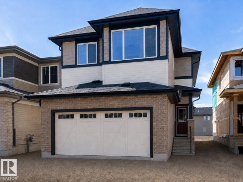 Contemporary two-story exterior featuring brick and siding, a two-car garage with white doors and transom windows, a dark shingle roof, and a covered entry with steps - 6275 180 Avenue Nw, Edmonton, AB - Outdoor