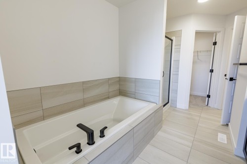 Soaking tub with matte black fixtures, surrounded by light-toned tile - 6275 180 Avenue Nw, Edmonton, AB - Indoor Photo Showing Bathroom