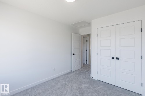 Recessed panel bi-fold closet doors with matte black hardware, light gray carpeting, and crisp white walls - 6275 180 Avenue Nw, Edmonton, AB - Indoor Photo Showing Other Room