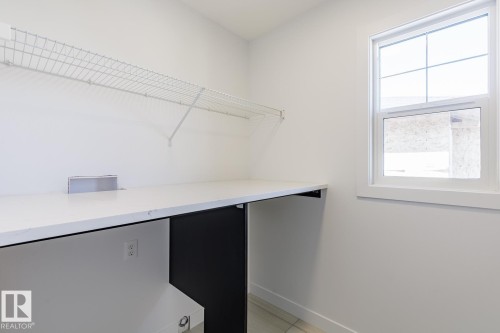 Laundry space featuring a white wire shelf, a large counter surface, a single window, and light-toned tile flooring - 6275 180 Avenue Nw, Edmonton, AB - Indoor With Storage