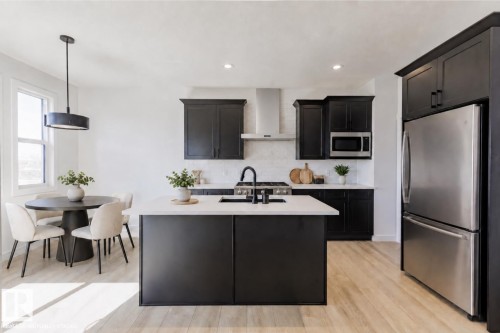 Modern kitchen featuring dark cabinetry, stainless steel appliances, a center island with a light-toned countertop, and wood-finish flooring - 6275 180 Avenue Nw, Edmonton, AB - Indoor Photo Showing Kitchen With Upgraded Kitchen