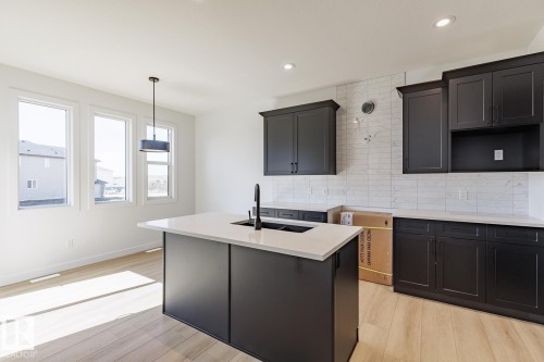 Contemporary kitchen featuring dark cabinetry, light countertops, wood-finish flooring, and a central island with an undermount sink - 6275 180 Avenue Nw, Edmonton, AB - Indoor Photo Showing Kitchen