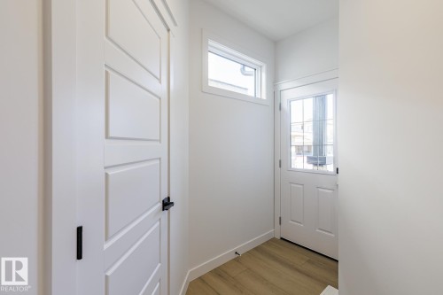 Entryway featuring a paneled door with matte black hardware, a glass-paned exterior door, and a transom window, complemented by wood-finish flooring - 6275 180 Avenue Nw, Edmonton, AB - Indoor Photo Showing Other Room
