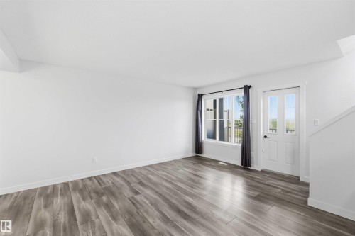 Spacious room featuring wood-finish flooring, white baseboards, and bright white walls - 36 1005 Graydon Hill Boulevard, Edmonton, AB 