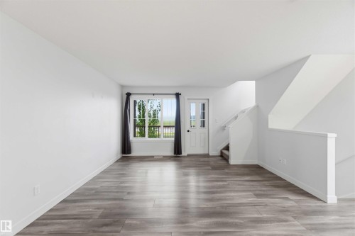 Spacious open-concept room featuring wood-finish flooring, white walls, and a large window with dark drapes - 36 1005 Graydon Hill Boulevard, Edmonton, AB 