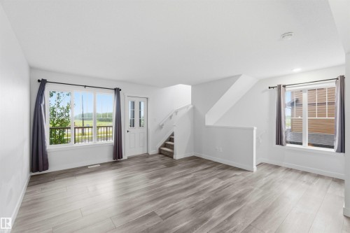 Open-concept room featuring light wood-finish flooring, white walls, and a staircase with carpeted treads - 36 1005 Graydon Hill Boulevard, Edmonton, AB 