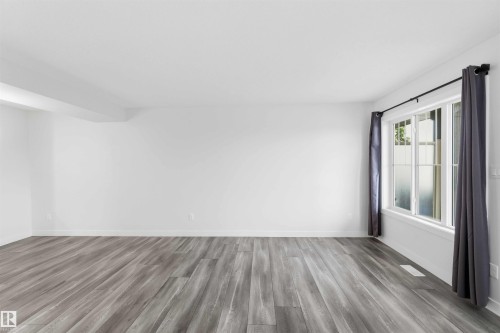 Spacious room featuring light wood-finish flooring, white baseboards, and bright white walls - 36 1005 Graydon Hill Boulevard, Edmonton, AB 