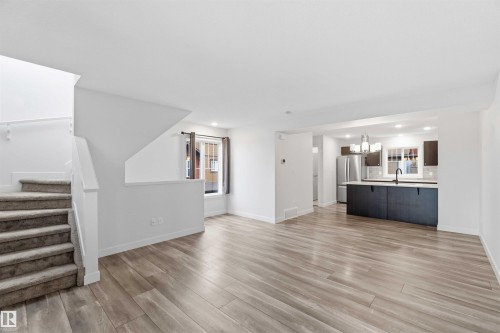 Open-concept living area featuring wood-finish flooring, a kitchen with dark cabinetry, stainless steel appliances, a white countertop, and contemporary pendant lighting - 36 1005 Graydon Hill Boulevard, Edmonton, AB 