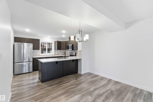 Open-concept kitchen and dining area featuring wood-finish flooring, dark wood cabinetry, stainless steel appliances, a kitchen island with seating potential, and a contemporary chandelier - 36 1005 Graydon Hill Boulevard, Edmonton, AB 