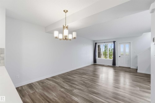 Open-concept living space with wood-finish flooring, white walls, and a contemporary brass chandelier - 36 1005 Graydon Hill Boulevard, Edmonton, AB 