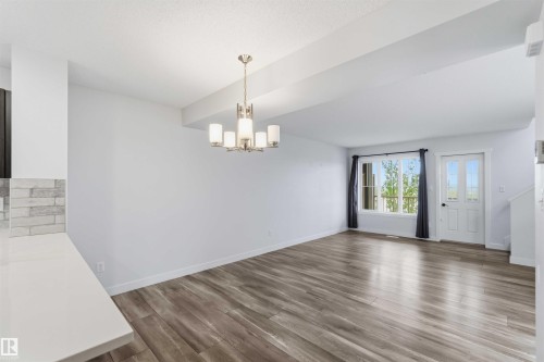 Open concept living space featuring wood-finish flooring, a contemporary chandelier, a large window, a white door with glass inserts, and a kitchen counter with a subway tile backsplash - 36 1005 Graydon Hill Boulevard, Edmonton, AB 