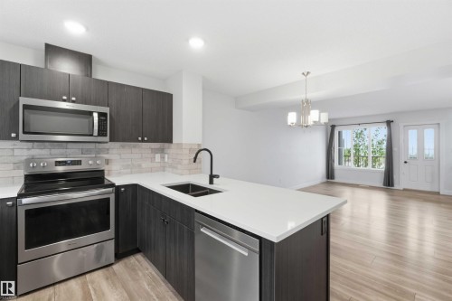 Contemporary kitchen featuring dark wood-finish cabinetry, stainless steel appliances, white countertops, and a subway tile backsplash - 36 1005 Graydon Hill Boulevard, Edmonton, AB 