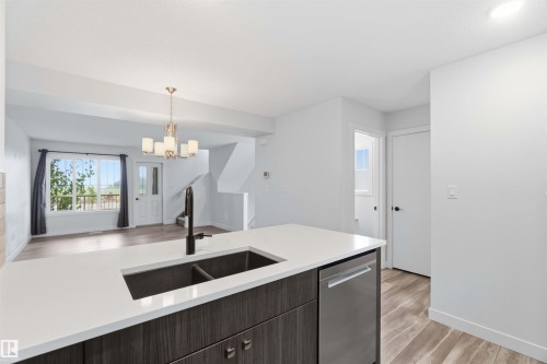 Contemporary kitchen island featuring a dual basin sink with a matte black faucet, integrated dishwasher, and white countertop - 36 1005 Graydon Hill Boulevard, Edmonton, AB 