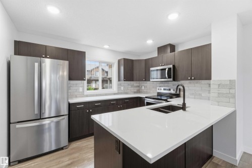 Kitchen featuring dark wood-finish cabinetry, stainless steel appliances, a white quartz island with an undermount sink, a white subway tile backsplash, and light wood-finish flooring - 36 1005 Graydon Hill Boulevard, Edmonton, AB 