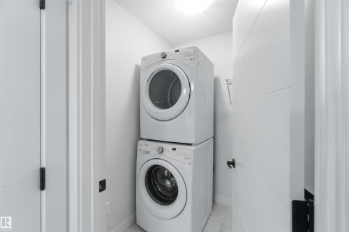 Laundry area featuring a stacked washer and dryer, white panel doors with black hardware, and bright overhead lighting - 36 1005 Graydon Hill Boulevard, Edmonton, AB 