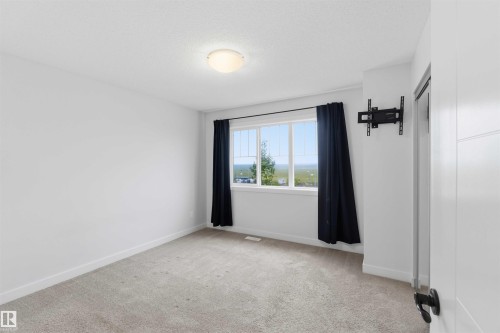 Carpeted room featuring a large window, white trim, and a flush-mount ceiling light - 36 1005 Graydon Hill Boulevard, Edmonton, AB 