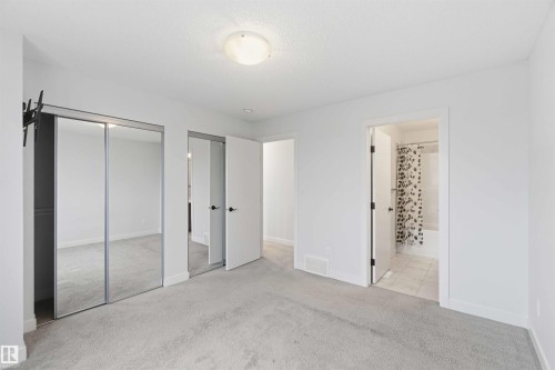Carpeted room featuring a ceiling-mounted light fixture, mirrored closet doors, white trim, and a door opening to a tiled bathroom with a shower-over-tub combination - 36 1005 Graydon Hill Boulevard, Edmonton, AB 