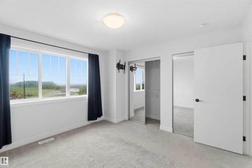 Bright room featuring a multi-pane window, wall-to-wall carpeting, a flush-mount ceiling light, and two sliding mirrored closet doors with wire shelving - 36 1005 Graydon Hill Boulevard, Edmonton, AB 