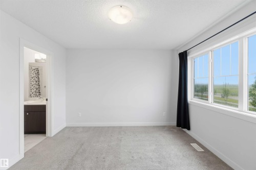 Carpeted room featuring a large multi-pane window, white walls, and a flush mount ceiling light - 36 1005 Graydon Hill Boulevard, Edmonton, AB 
