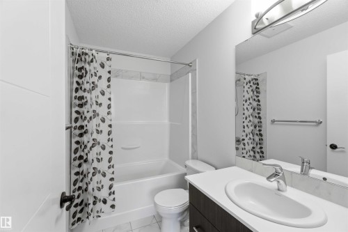 Bathroom featuring a white bathtub and shower surround with tile accent, a white toilet, and a vanity with a white countertop and undermount sink - 36 1005 Graydon Hill Boulevard, Edmonton, AB 