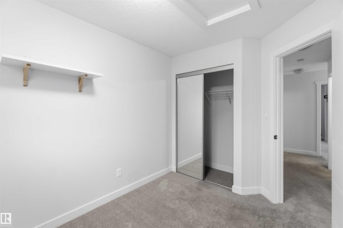 Carpeted room featuring a white wall shelf with wood brackets, a closet with mirrored sliding doors, and white baseboards - 36 1005 Graydon Hill Boulevard, Edmonton, AB 