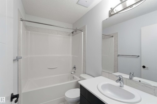 Bathroom featuring a white tub/shower combination with tile surround, a dark wood-finish vanity with a white countertop, an undermount sink, and a large wall mirror - 36 1005 Graydon Hill Boulevard, Edmonton, AB 