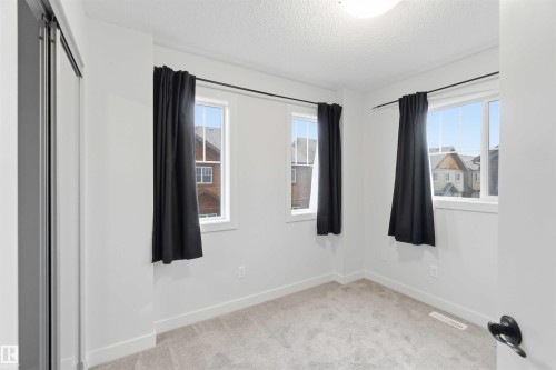 Room featuring light gray carpet, white walls, multiple windows with dark drapery, and a white ceiling light fixture - 36 1005 Graydon Hill Boulevard, Edmonton, AB 