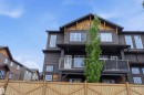 Multi-story residential exterior featuring dark horizontal siding, light wood-finish gables, multiple window styles, a second-story balcony with metal railings, and a wood privacy fence - 36 1005 Graydon Hill Boulevard, Edmonton, AB 