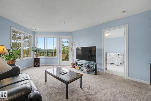 Bright living area featuring multiple large windows and a glass-paneled door opening to an exterior balcony - 303 530 Hooke Road, Edmonton, AB - Indoor Photo Showing Living Room