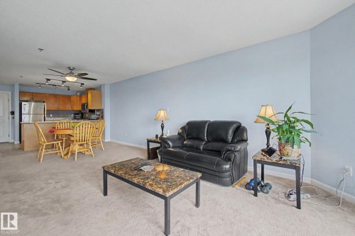 Open-concept living space featuring a kitchen with wood cabinetry, stainless steel refrigerator, and a breakfast bar - 303 530 Hooke Road, Edmonton, AB - Indoor Photo Showing Living Room
