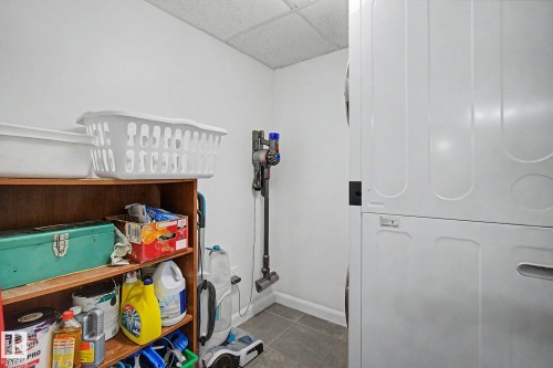 Dedicated laundry area featuring a white stackable washer and dryer, white walls, and gray tile flooring - 303 530 Hooke Road, Edmonton, AB - Indoor Photo Showing Other Room