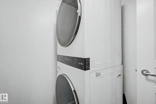 Stackable white washer and dryer unit with front-loading doors and digital controls - 303 530 Hooke Road, Edmonton, AB - Indoor Photo Showing Laundry Room