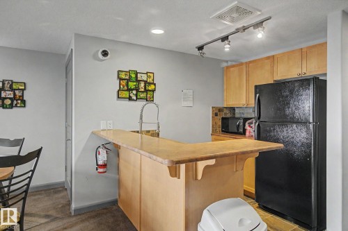 Kitchenette featuring light wood-finish cabinetry, black appliances, a tile backsplash, and track lighting - 303 530 Hooke Road, Edmonton, AB - Indoor Photo Showing Other Room