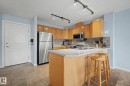 Kitchen featuring light wood cabinetry, stainless steel appliances, a counter-height island with seating space, and tile flooring - 303 530 Hooke Road, Edmonton, AB  - Indoor Photo Showing Kitchen 