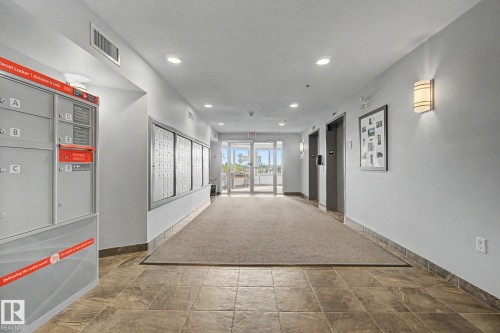 Building corridor with recessed lighting, wall sconces, parcel lockers, individual mailboxes, and two elevator doors - 303 530 Hooke Road, Edmonton, AB - Indoor Photo Showing Other Room