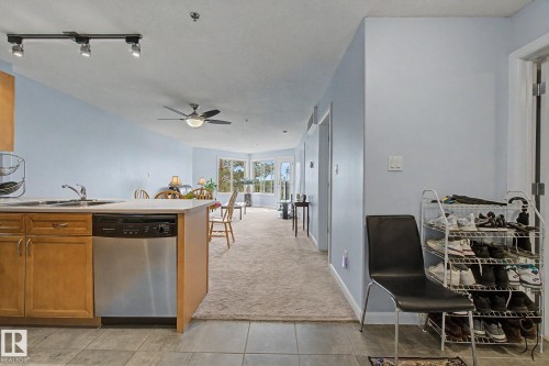 Open-concept living area featuring a kitchen island with sink and stainless steel dishwasher, track lighting, and a ceiling fan - 303 530 Hooke Road, Edmonton, AB - Indoor Photo Showing Kitchen With Double Sink