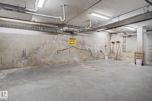 Concrete floor and unfinished concrete walls with exposed ductwork and fluorescent lighting - 303 530 Hooke Road, Edmonton, AB - Indoor Photo Showing Garage