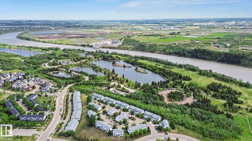 Aerial perspective showcasing a community with numerous water features, abundant green spaces, and a winding river - 303 530 Hooke Road, Edmonton, AB - Outdoor With View