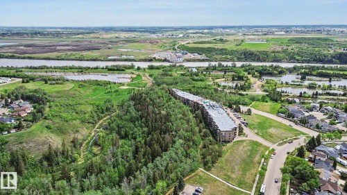 Multi-story residential building situated amidst mature trees, featuring a paved parking area - 303 530 Hooke Road, Edmonton, AB - Outdoor With View