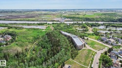 Multi-story residential building situated amidst mature trees, featuring a paved parking area - 