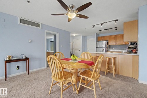 Dining area featuring a ceiling fan with integrated lighting, soft blue walls, and light-toned carpet flooring - 303 530 Hooke Road, Edmonton, AB - Indoor