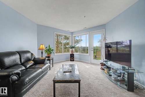 Light blue walls complement the light-toned carpet flooring - 303 530 Hooke Road, Edmonton, AB - Indoor Photo Showing Living Room
