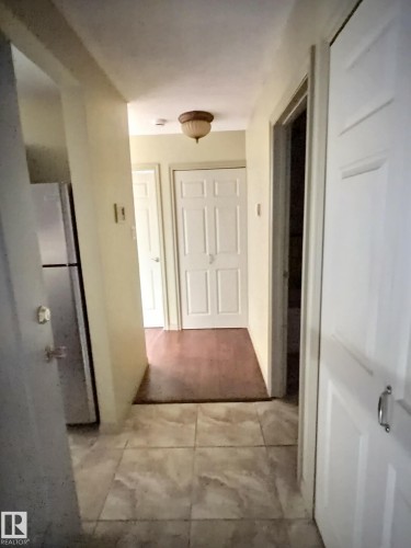 Hallway featuring light-toned tile flooring transitioning to wood-finish flooring - 306 9730 156 Street, Edmonton, AB 