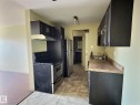 Compact kitchen featuring dark cabinetry with brushed nickel hardware, a stainless steel sink, and a speckled countertop - 306 9730 156 Street, Edmonton, AB 
