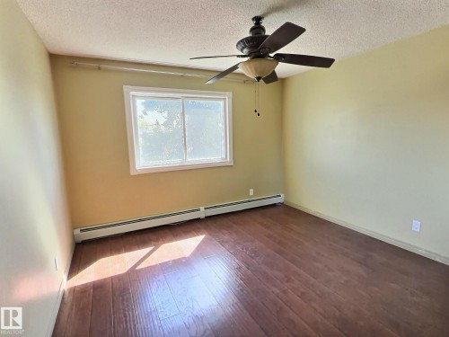 Spacious room featuring wood-finish flooring, light yellow walls, and a white-framed window - 306 9730 156 Street, Edmonton, AB 