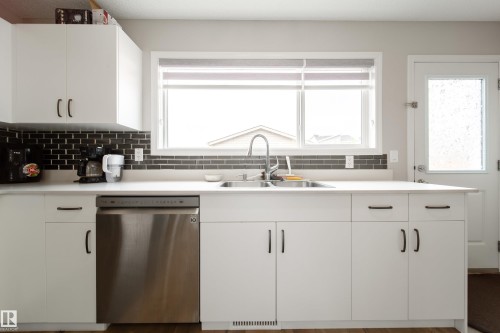 Kitchen featuring white cabinetry with dark hardware, a dark subway tile backsplash, white countertops, and a stainless steel dishwasher - 3038 Checknita Way Sw, Edmonton, AB 